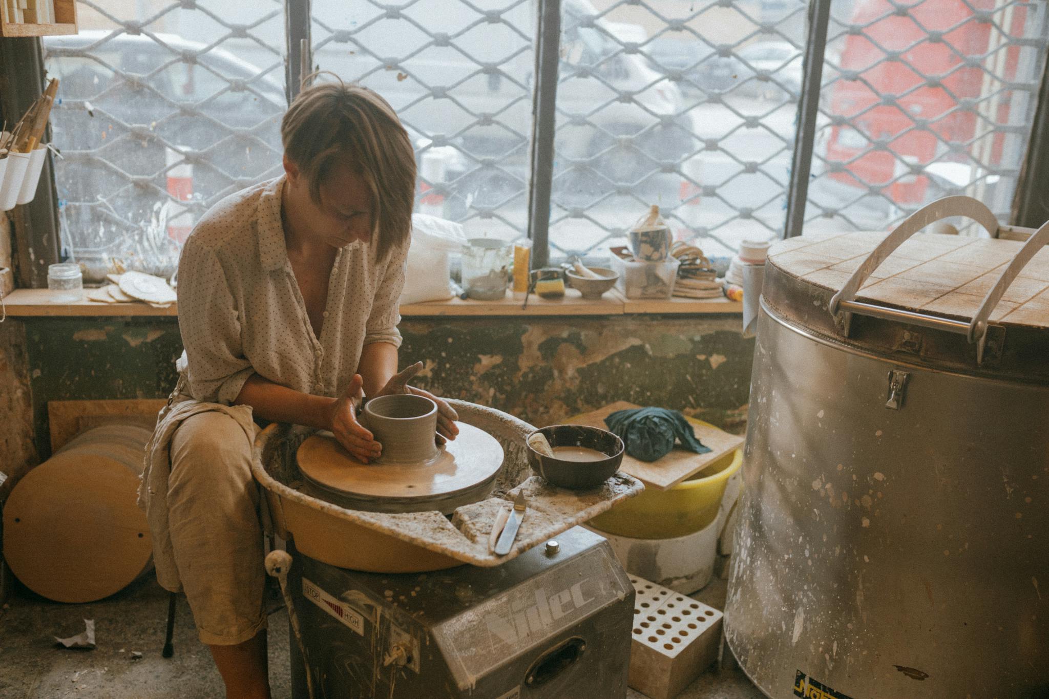 A focused artisan skillfully shapes clay on a pottery wheel in a rustic workshop setting.