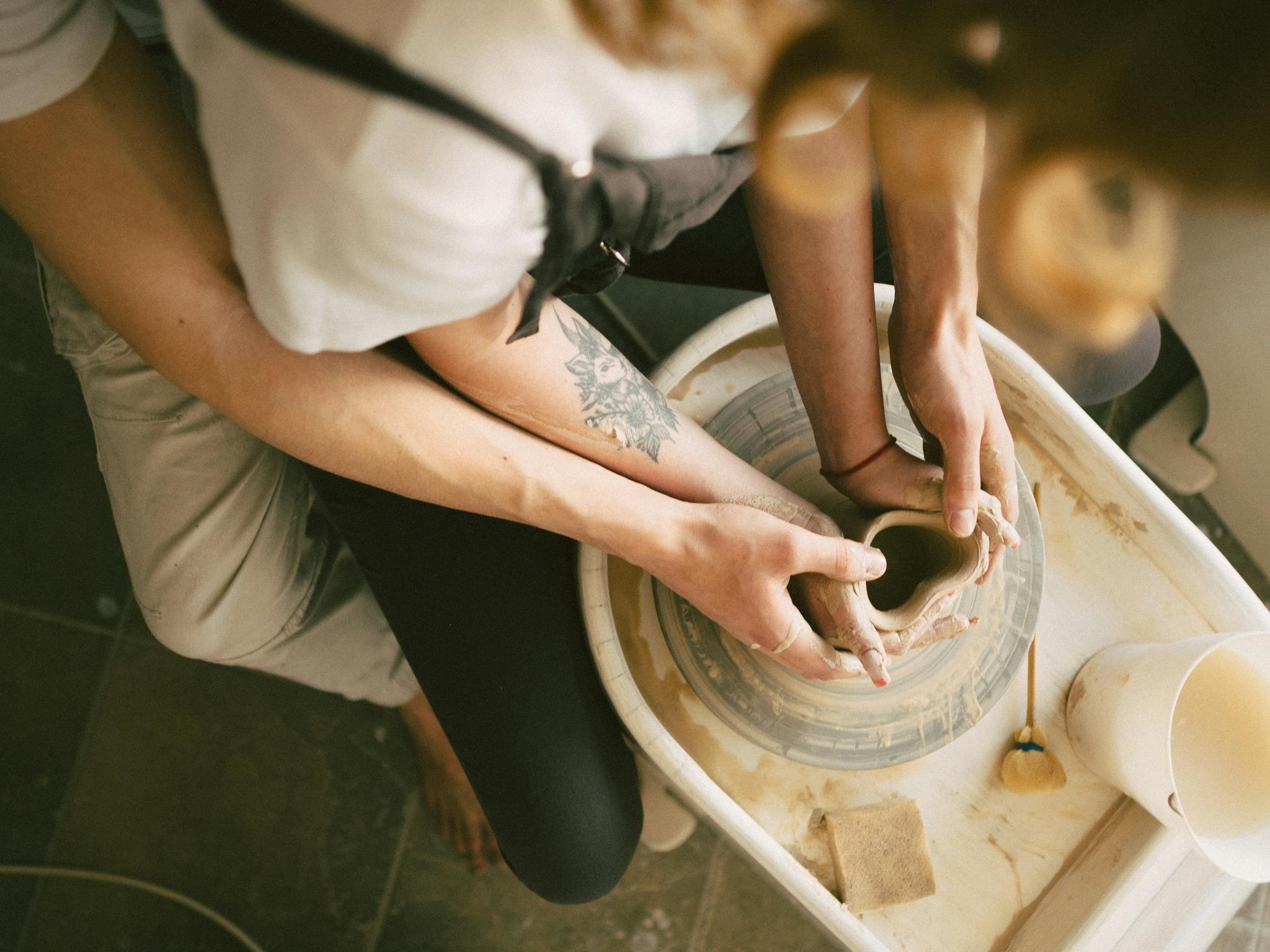 Close-up of two people shaping clay on a pottery wheel, creating art together.